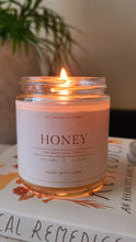 Load image into Gallery viewer, lit beeswax candle in glass jar atop books