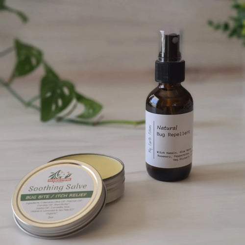 2 ounce metal tin of Soothing salve next to a glass jar of bug repellent spray with green plant in the background